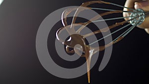 Chocolate flows from the whisk when mixed with cream on a black background 4k.