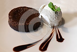 A chocolate fondant cake with a ball of vanilla ice cream on a white plate decorated with liquid chocolate