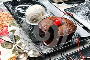 Chocolate fondant cake with ice cream and cherries in plate on wooden background. Sweets, dessert and pastry, close up