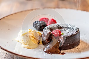 Chocolate fondant cupcake with raspberries, ice creme and powdered sugar placed on plate