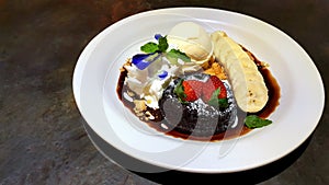 Chocolate fondant lava cake decorated by sprinkling of icing sugar, fresh strawberries, banana and ice cream