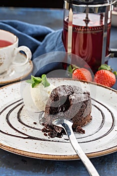 Chocolate fondant lava cake decorated with vanilla ice cream and cup of tea on blue background
