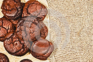 Chocolate freshly baked cookies, layout out on a paper pad and their burlap background. Top view of brownie cookies with copy