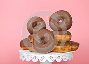 Chocolate glazed donuts stacked on white pedestal pink background close up