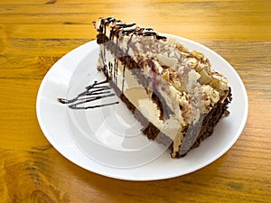 Chocolate hazelnut cake slice with drizzle on white plate on wooden table