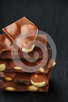 Chocolate with hazelnut in the form of a tower on a dark background. Pieces of milk chocolate with nuts