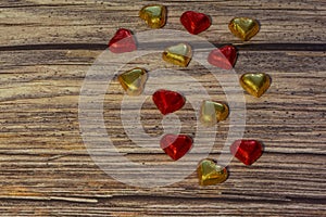Chocolate hearts in gold and red foil on a brown wooden background. Valentine's Day, greeting card. Copy space, top view photo