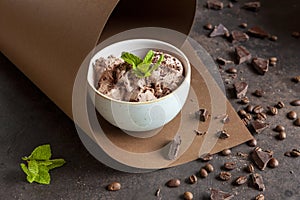 Chocolate ice cream with chocolate chips, coffee beans and fresh mint in paper swirl on brown background