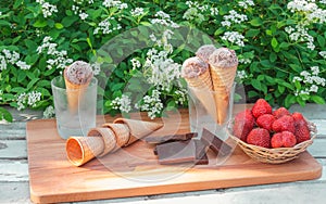 Chocolate ice cream, dark chocolate, fresh strawberry and empty waffle cones on rustic wooden table