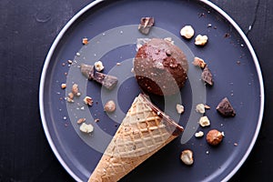 Chocolate ice cream with hazelnuts in a cone on a dark plate