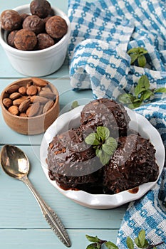 Chocolate ice cream with liquid chocolate and with a cinnamon stick, coffee beans and almonds on a blue wooden background