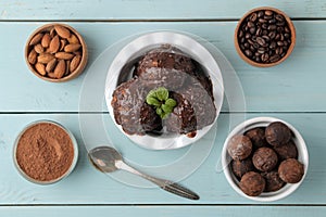 Chocolate ice cream with liquid chocolate and with a cinnamon stick, coffee beans and almonds on a blue wooden background. top vie