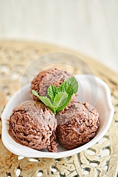 Chocolate ice cream with mint leafe. three balls in a white bowl on a vintage table.