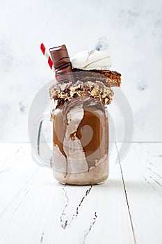 Chocolate indulgent exreme milkshake with brownie cake, marshmallow and sweets. Crazy freakshake food trend.