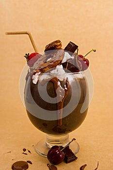 Chocolate indulgent extreme milkshake with brownie cake, strawberries, cherries, and a plastic straw with milk foam on