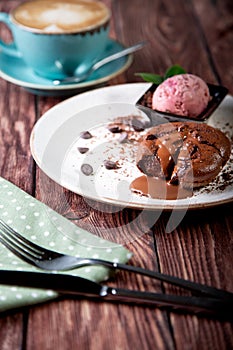 Chocolate lava cake Molten with ice cream on plate and cappuccino. Balls of ice cream in cup . Dark black background.