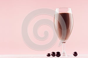 Chocolate milkshake in elegance glass with chocolate candies on white wooden table and pastel light pink wall.