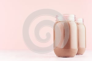 Chocolate milkshake in two stylish jars on white wooden table and pastel light pink wall.