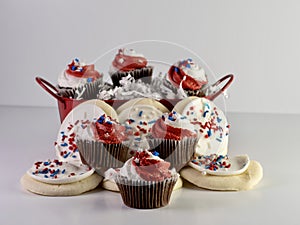 Chocolate mini cupcakes with red and white frosting and star sprinkles along with sugar cookies with white frosting and red, white