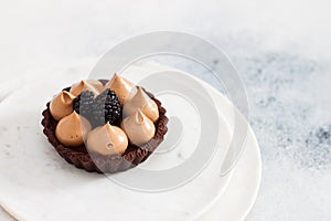 Chocolate mini tart with whipped caramel cream and fresh blackberry. Plain white background.