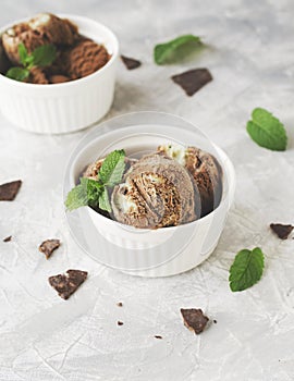 Chocolate mint ice cream in white bowls with pieces of chocolate and mint leaves on a marble table