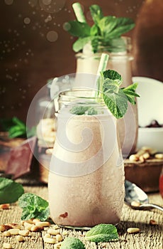 Chocolate mint smoothies or milk cocktails with cedar nuts in glass bottles on old wooden kitchen table background, selective