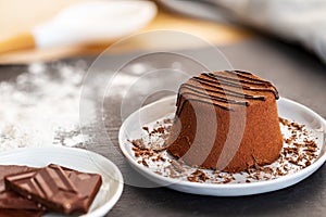 Chocolate Moelleux cake or molten cake in a grey plate with grated chocolate, spilled flour and chocolate pieces on a slate
