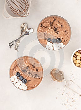 Chocolate mousse dessert placed on white background with hazelnuts, dark chocolate, blueberries, top view, flat lay.