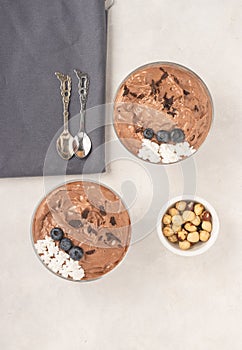 Chocolate mousse dessert placed on white background with hazelnuts, dark chocolate, blueberries, top view, flat lay.