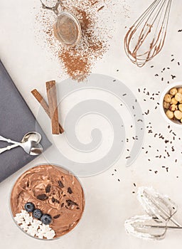 Chocolate mousse dessert placed on white background with hazelnuts, dark chocolate, blueberries, top view, flat lay.