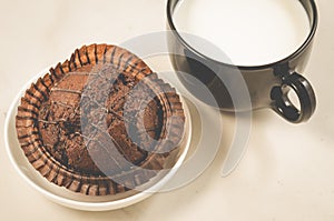 Chocolate muffin and milk/chocolate muffin and a black mug with milk on a white. Top view