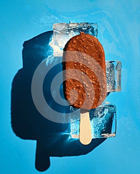 Chocolate nut ice cream on ice cubes on a blue background. Sunlight. Summer concept