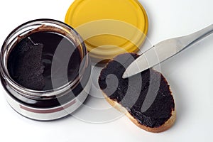 Chocolate paste in a glass jar next to a slice of white bread and a knife