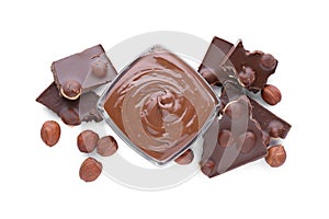 Chocolate pieces, bowl of sweet paste and hazelnuts on white background, top view