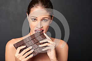 Chocolate, portrait and woman in studio eating for unhealthy diet, craving sugar or cheat day on dark background. Bite