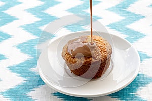 Chocolate is poured onto cake at plate on striped background.