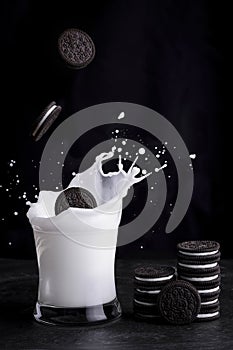 Chocolate sandwich cookies with sweet cream flavour filling dropped in fresh milk splash in glass on dark table