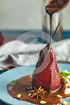Chocolate sauce pours from a spoon on red pears in wine
