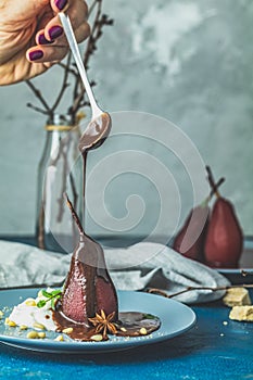 Chocolate sauce pours from a spoon on red pears in wine