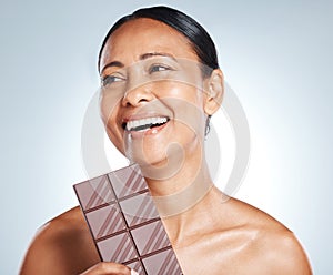 Chocolate, smile and senior woman thinking of health isolated on a blue background in studio. Food, happy and face of an