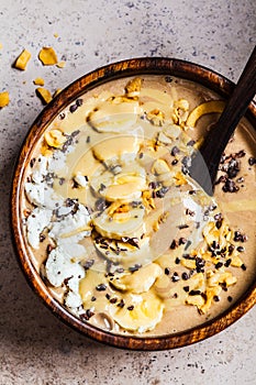 Chocolate smoothie bowl with coconut chips, banana and cocoa nibs in wooden bowl, top view. Healthy vegetarian breakfast concept