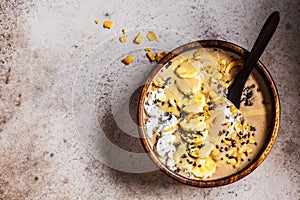 Chocolate smoothie bowl with coconut chips, banana and cocoa nibs in wooden bowl, top view. Healthy vegetarian breakfast concept