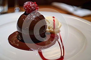 Chocolate Sphere, Passionfruit coulis cascades down, vanilla ice cream rests beside it photo