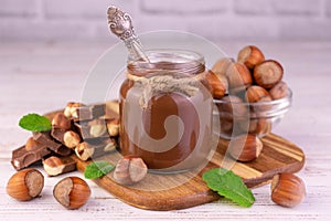 Chocolate spread with hazelnuts in a jar on a white wooden background.