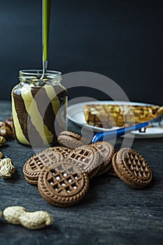 Chocolate spread or nougat cream with hazelnuts in a glass jar on a dark wooden background