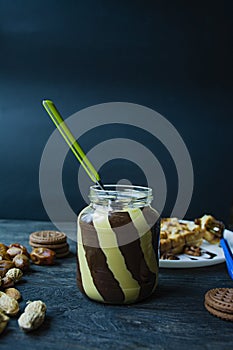 Chocolate spread or nougat cream with hazelnuts in a glass jar on a dark wooden background