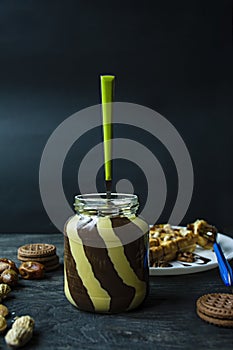 Chocolate spread or nougat cream with hazelnuts in a glass jar on a dark wooden background