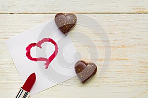 Chocolate sweets in hear shape abd note with red lipstic painted heart on a paper. Consept of love and valentines day