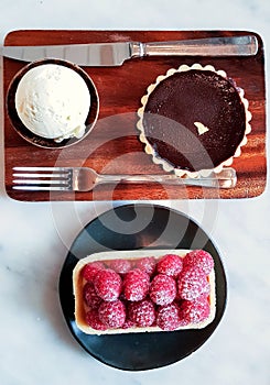 Chocolate Tart with a scoop of vanilla ice cream served on wooden plate and Raspberry Tart served on black porcelain plate.