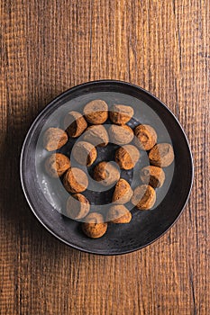 Chocolate truffles covered with cocoa powder on plate on wooden table. Top view